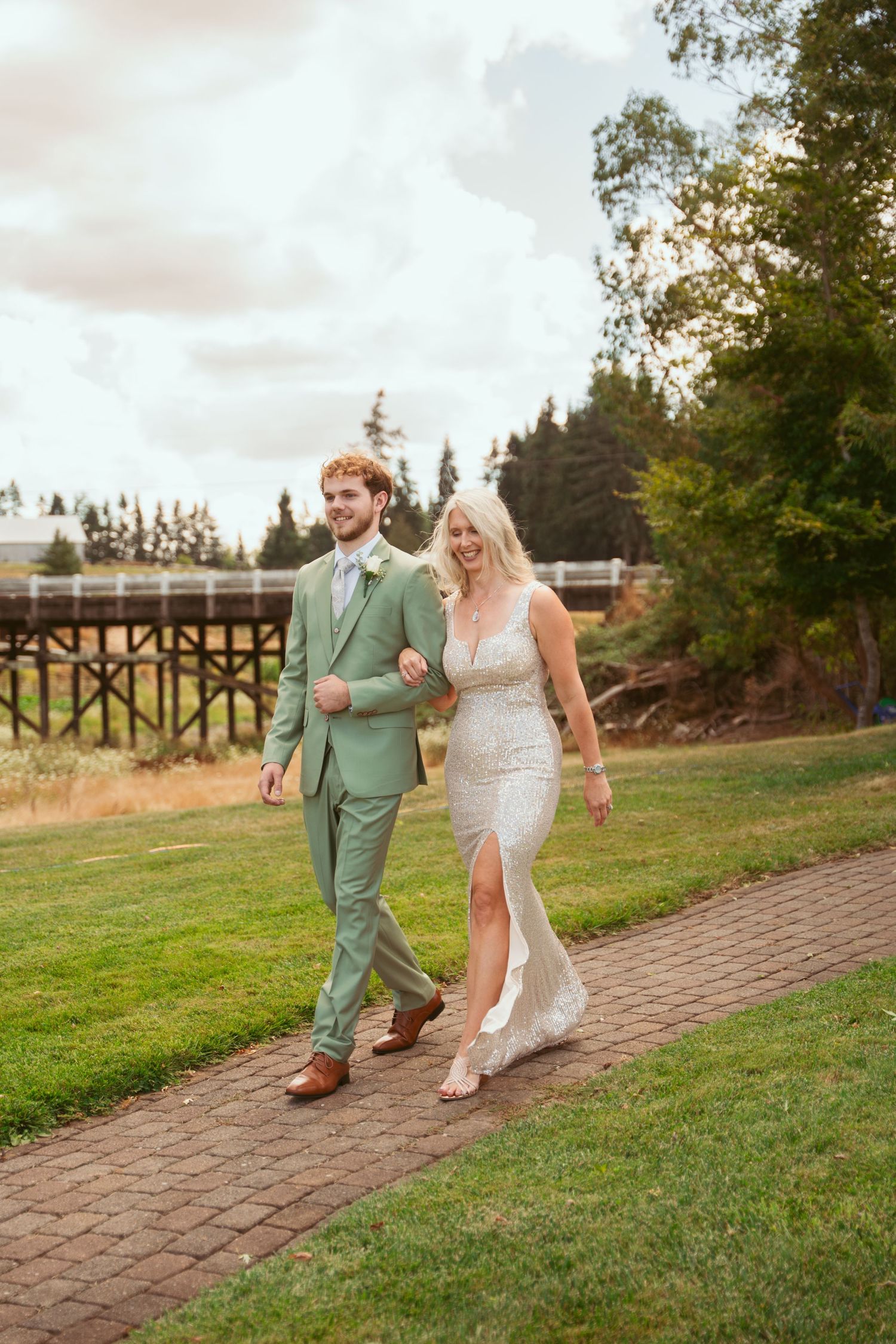 A couple walks along a brick pathway on a grassy hillside during their wedding.