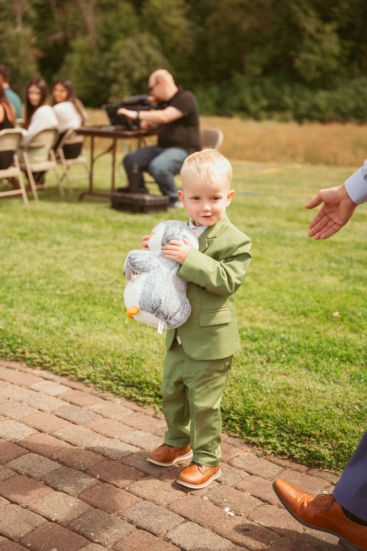 A small child in a green outfit takes first steps on a brick pathway in an outdoor setting.