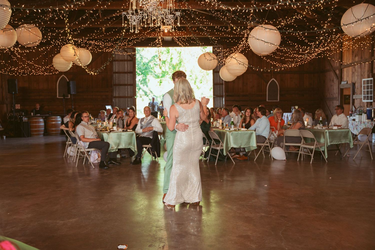 Couple performs special dance moves in barn reception venue with string lights and paper lanterns.