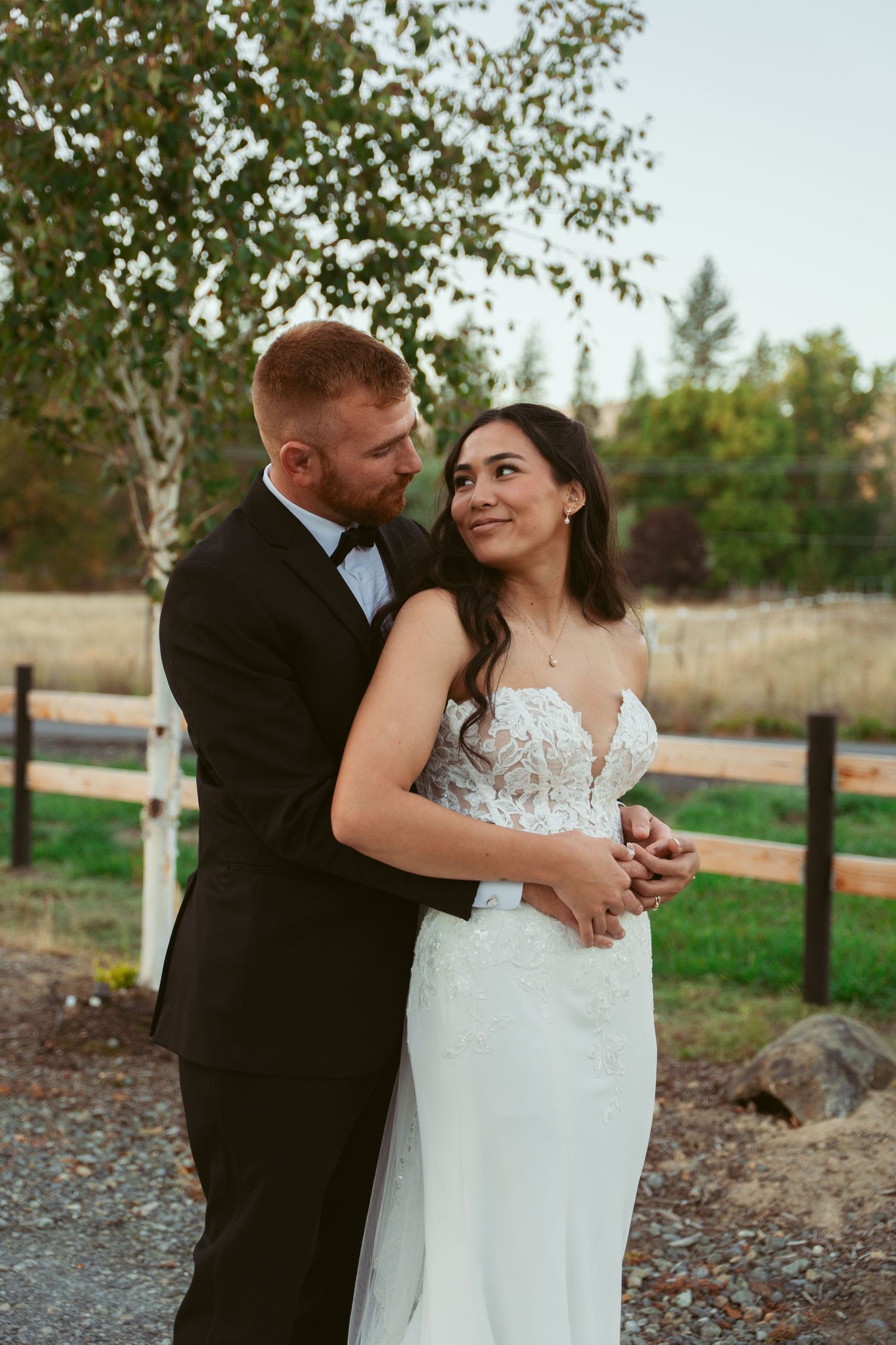 Romantic newlyweds embrace on their wedding day against a rustic outdoor backdrop with birch trees.