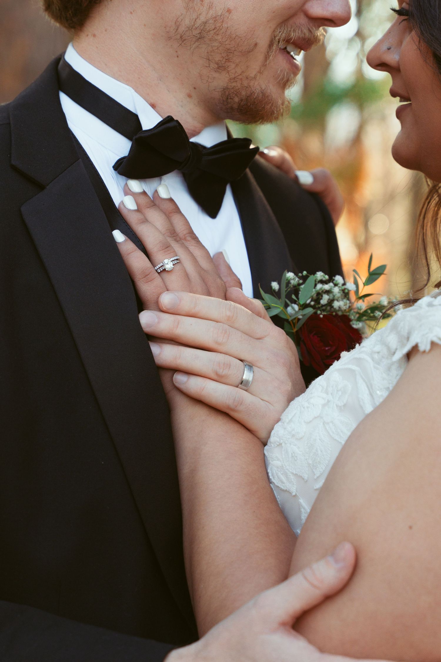 A close-up wedding photo showing wedding rings, boutonniere, and formal attire details.