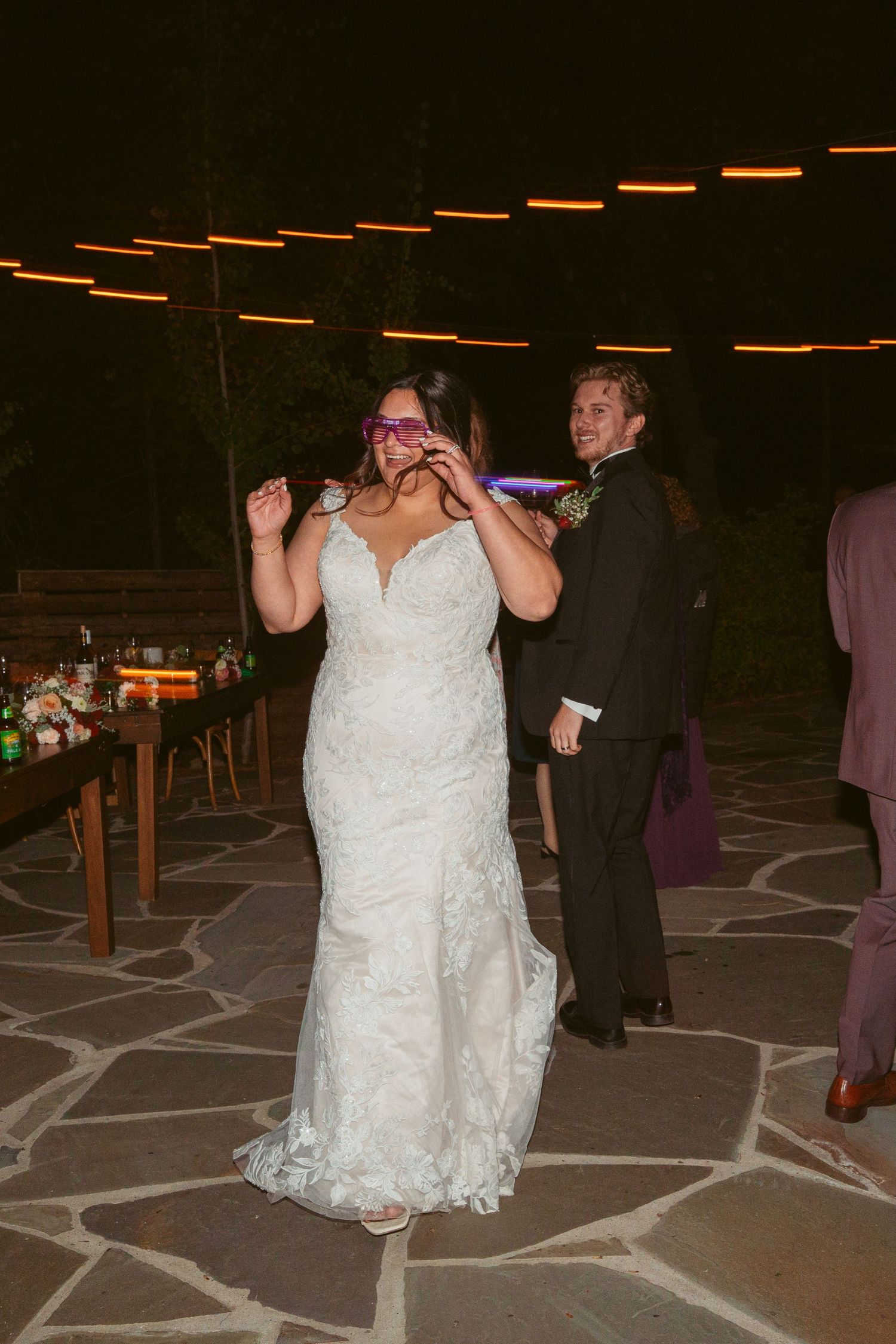 A couple dances together on a patterned stone patio under string lights at night.