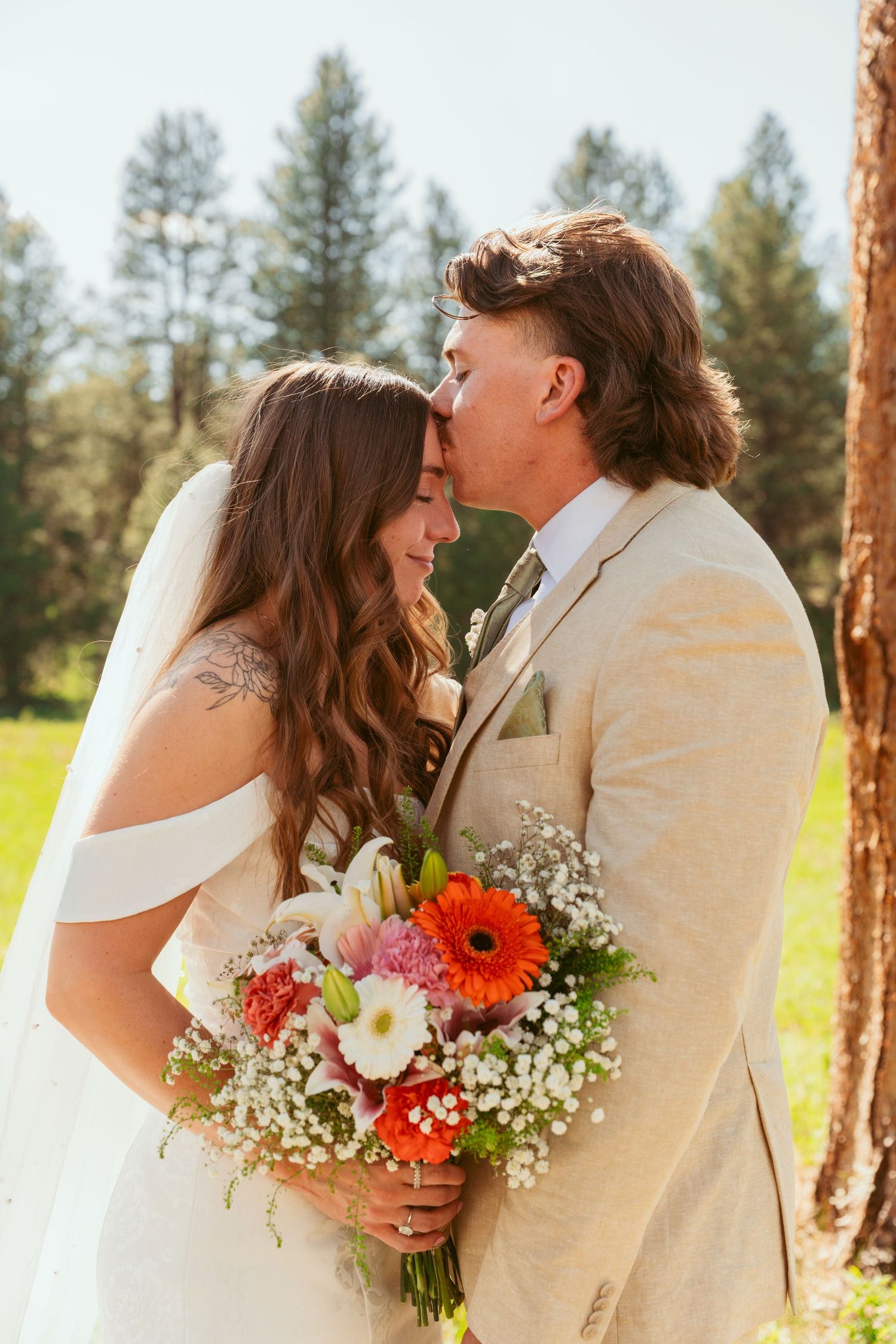 A tender wedding portrait with a vibrant bouquet of red and white flowers against a natural forest backdrop.