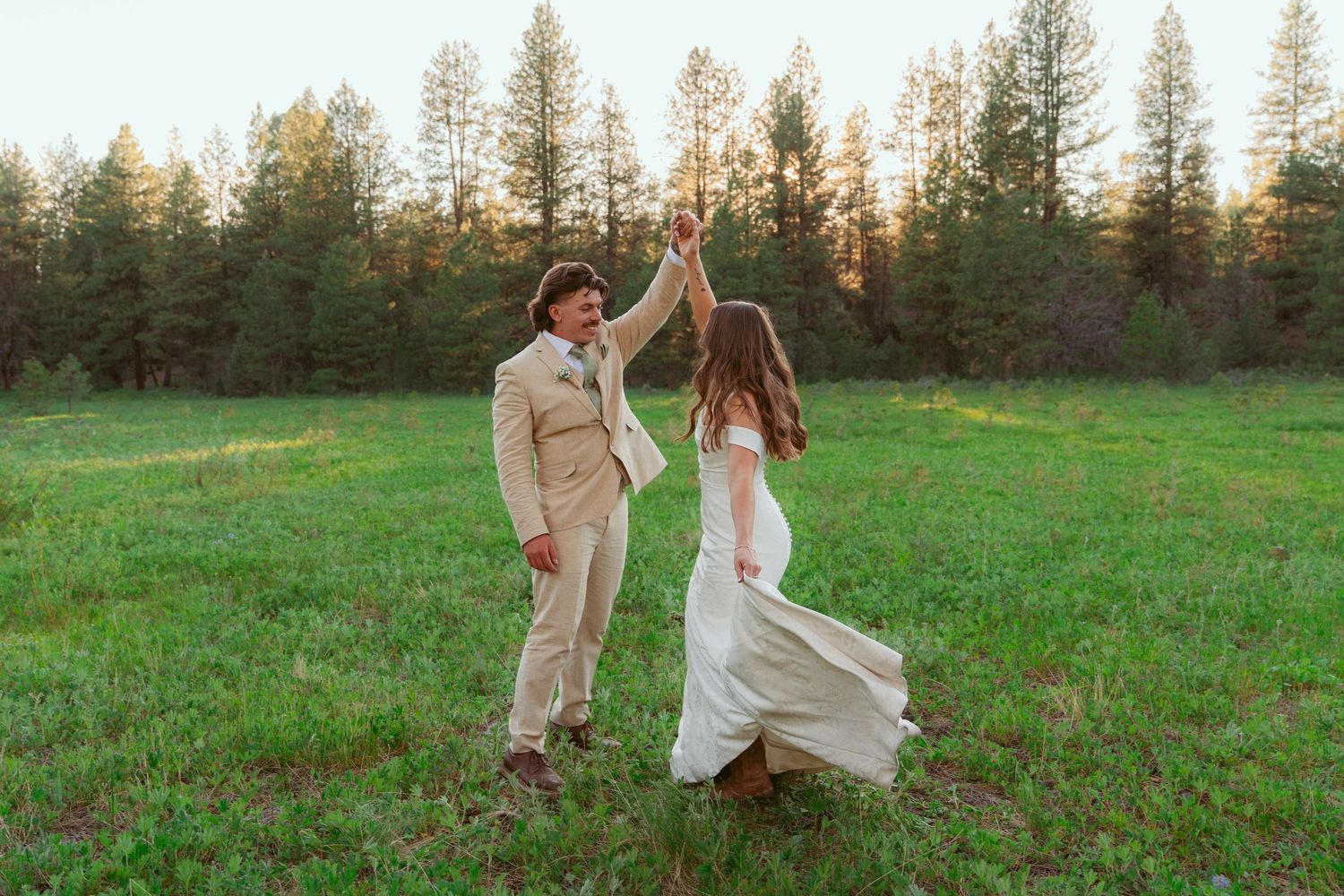 Joyful couple dancing together in a grassy field during golden hour.