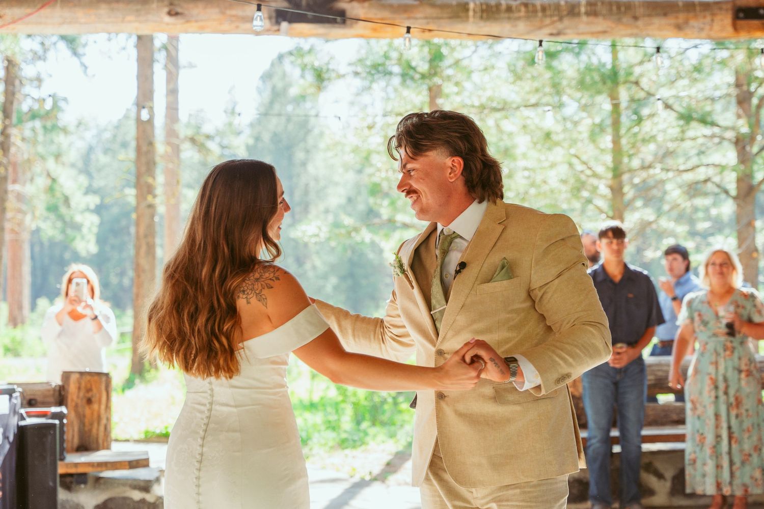Couple shares a dance in sunlit wooden pavilion during their wedding celebration.