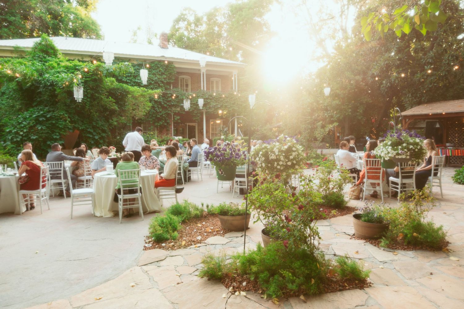 Panoramic view of an outdoor wedding reception with string lights and white chairs.