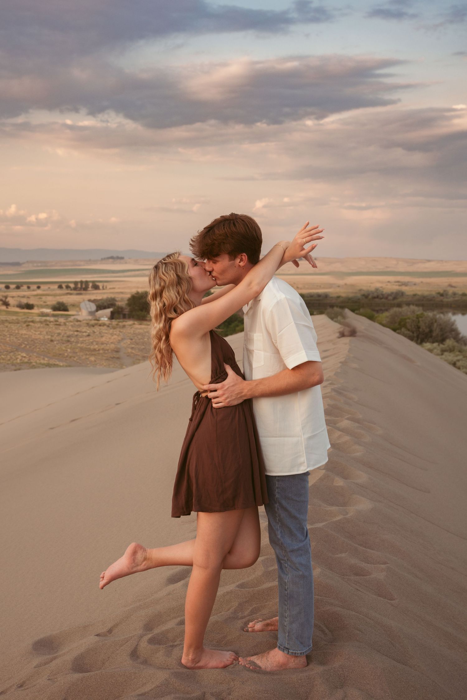 Romantic couple embracing on sand dunes during golden hour photography session.