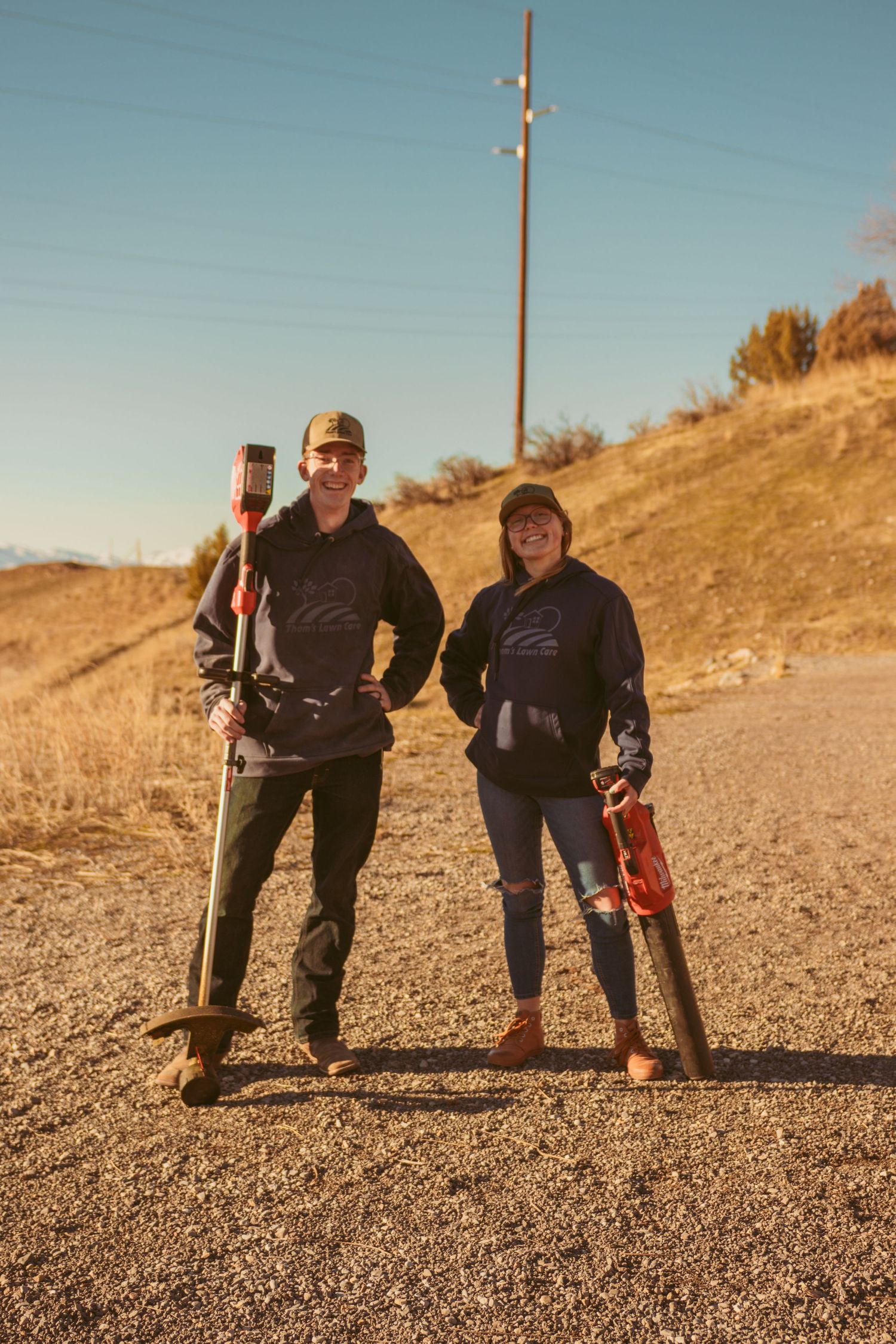 Two people playfully posing together on a gravel path with mountains in the background.