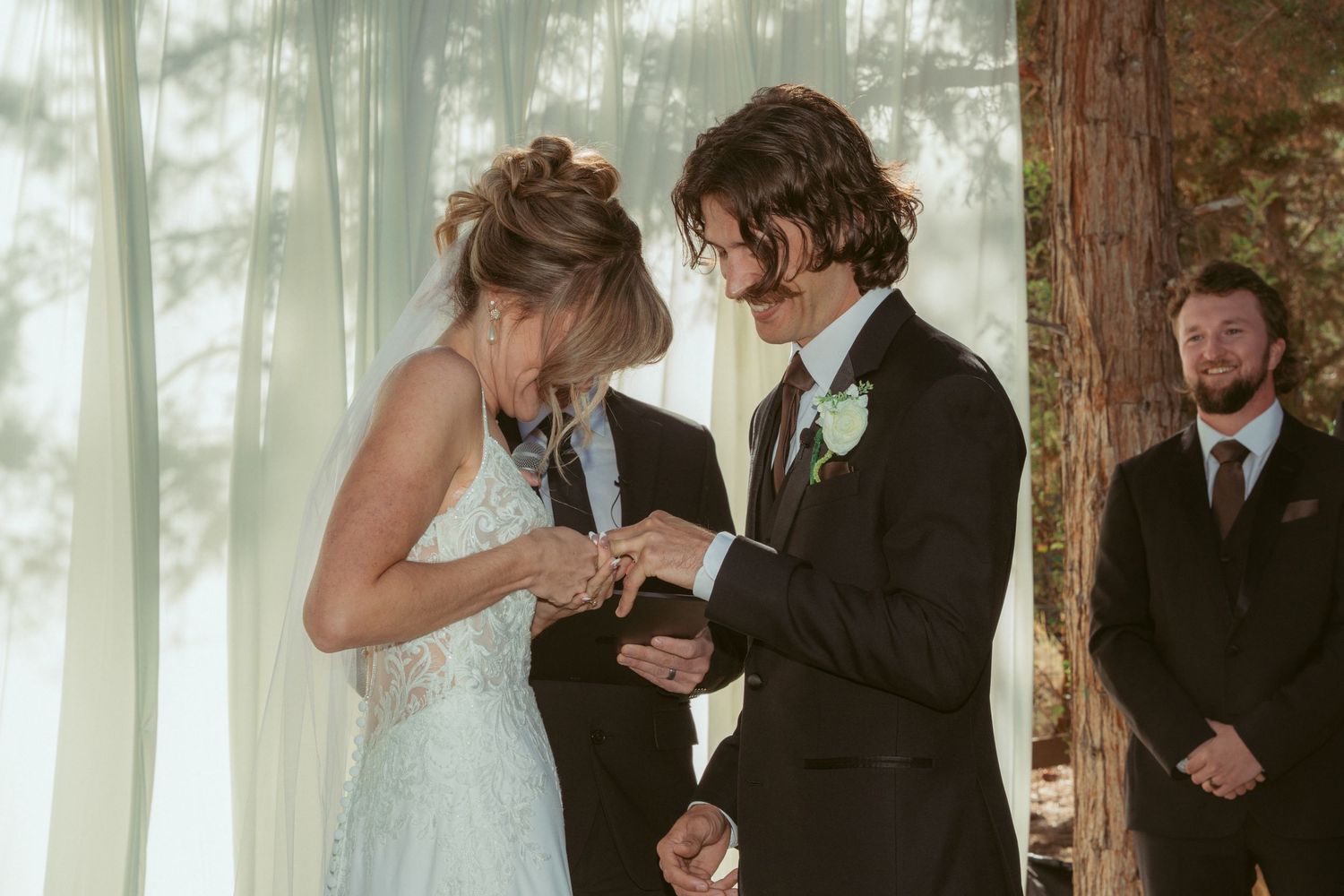 Emotional ring exchange moment during outdoor forest wedding ceremony.