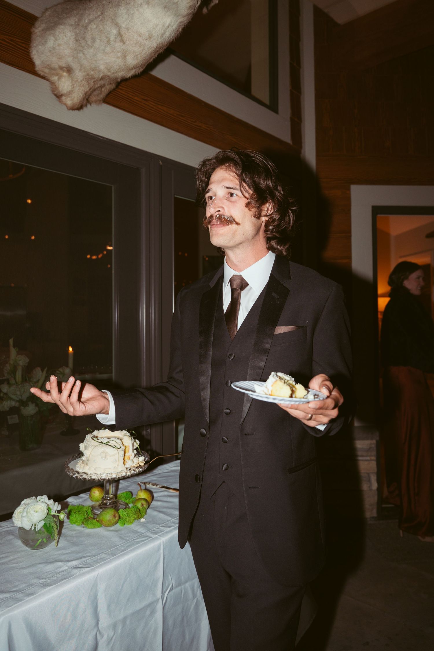 A couple in formal attire shares cake at an indoor wedding reception.