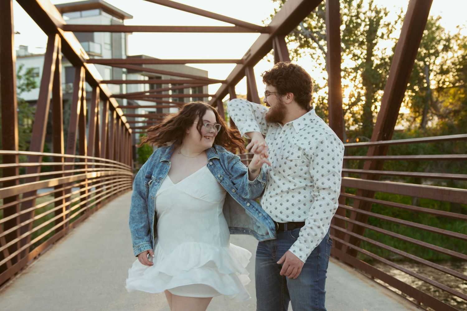 A couple dancing playfully on a wooden bridge during golden hour.