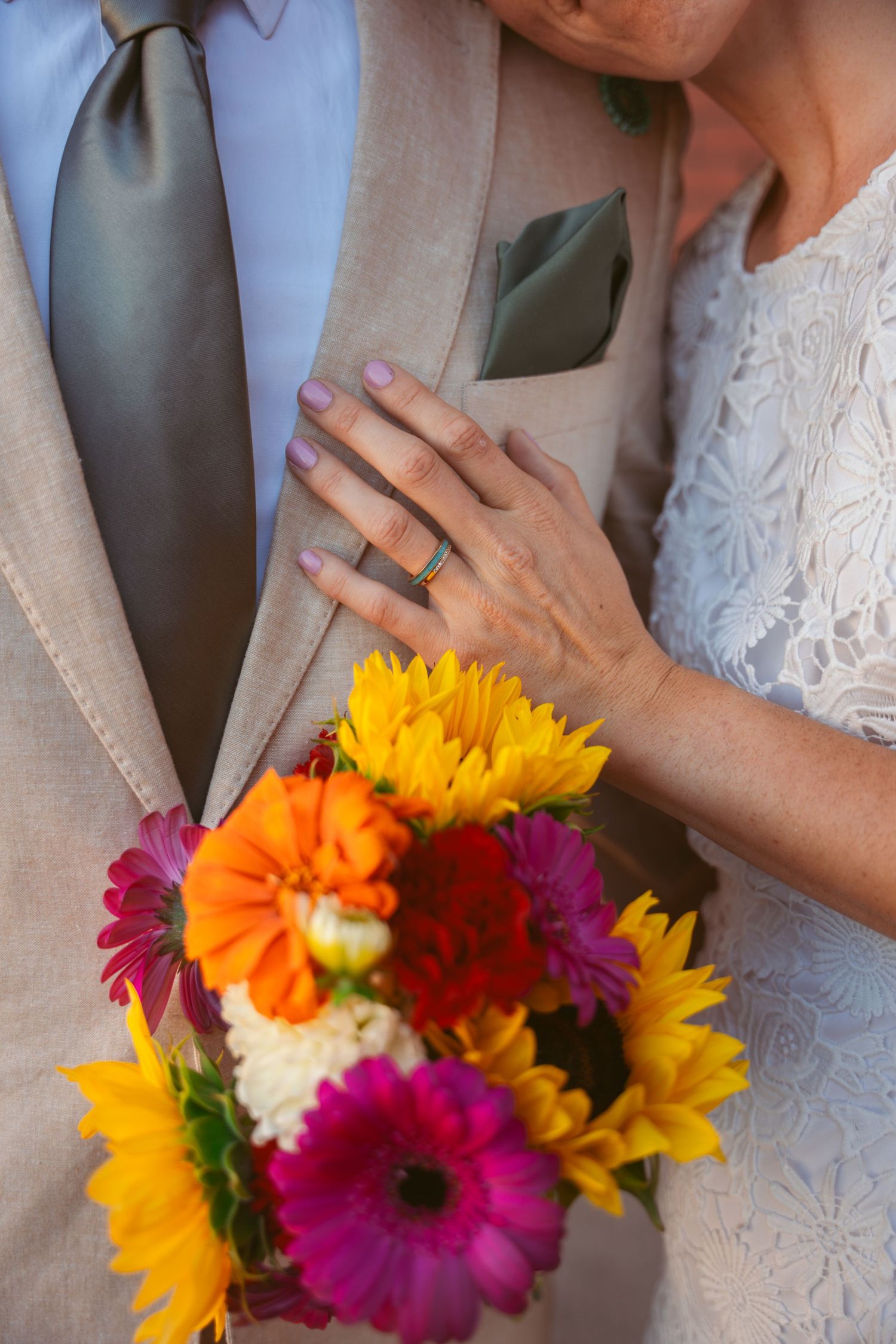 Close-up of vibrant wedding bouquet with sunflowers and pink gerbera daisies against formal attire.