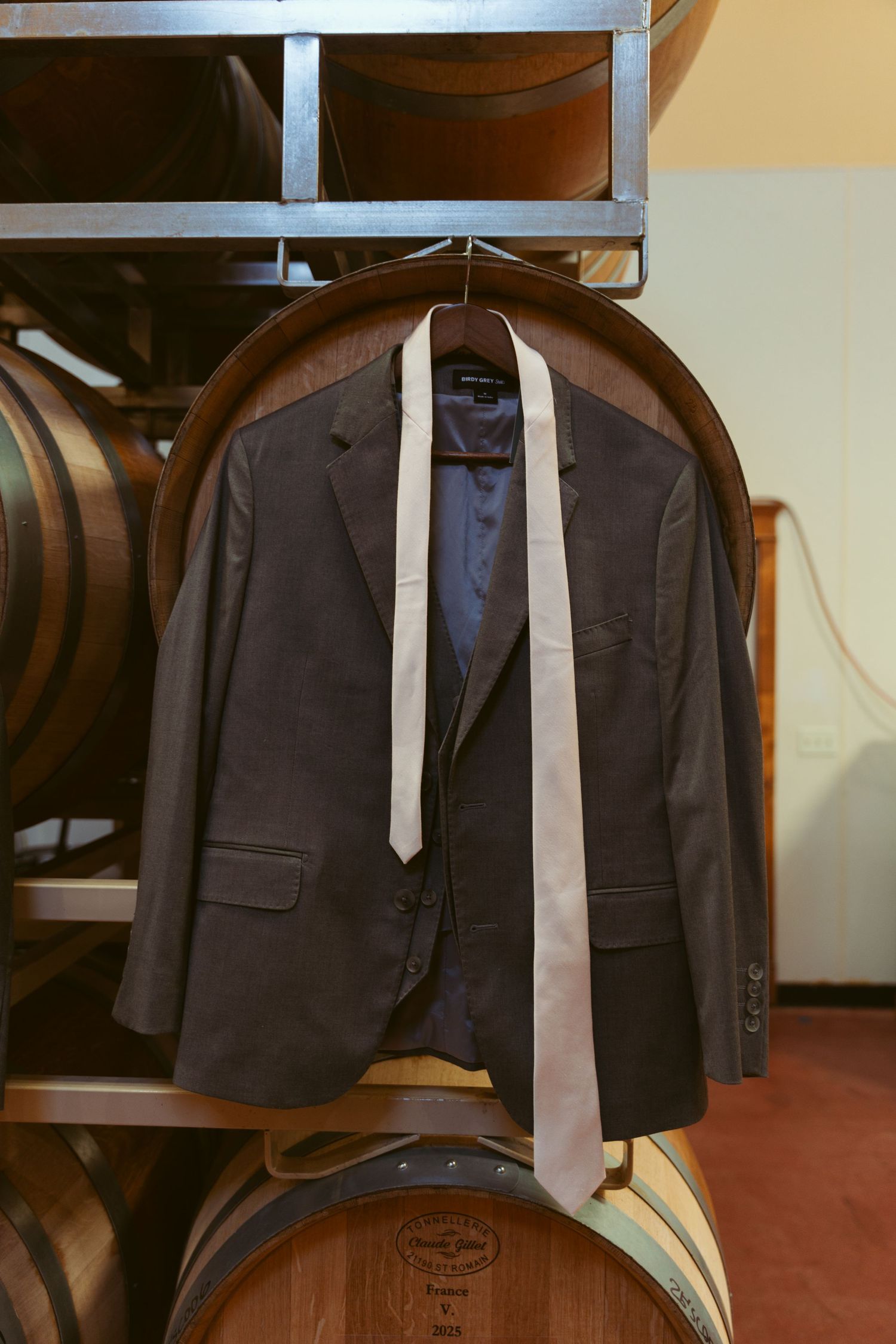 Dark suit jacket and tie hanging on display in front of wine barrels.