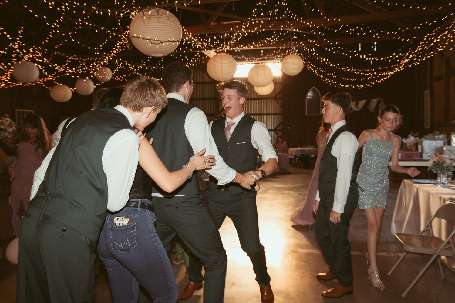 Wedding celebration in full swing with dancing guests under warm lighting and paper lanterns.