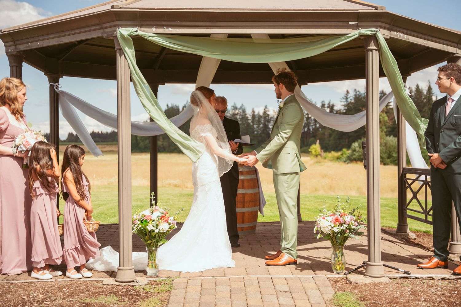 Panoramic view of an outdoor wedding ceremony under a wooden pavilion with guests seated on both sides.