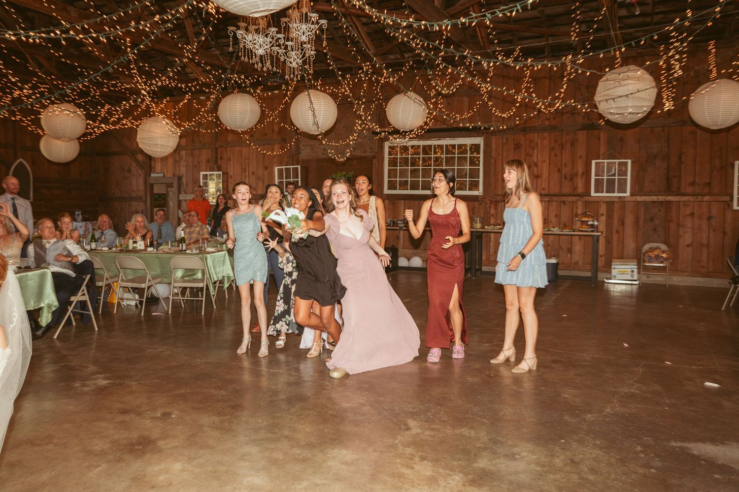 Wedding reception dance party in a rustic barn decorated with glowing string lights and paper lanterns.
