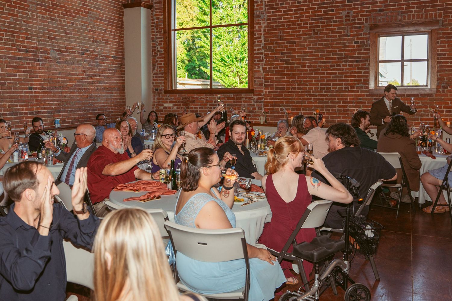 Wedding guests celebrating with raised glasses in an industrial brick venue.