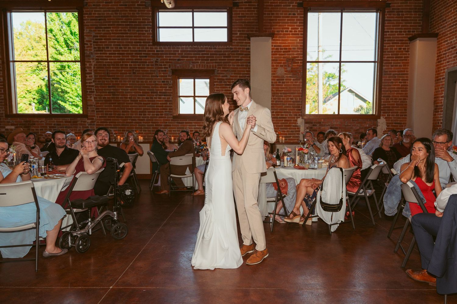 Wedding celebration in historic brick venue with guests seated around dance floor.