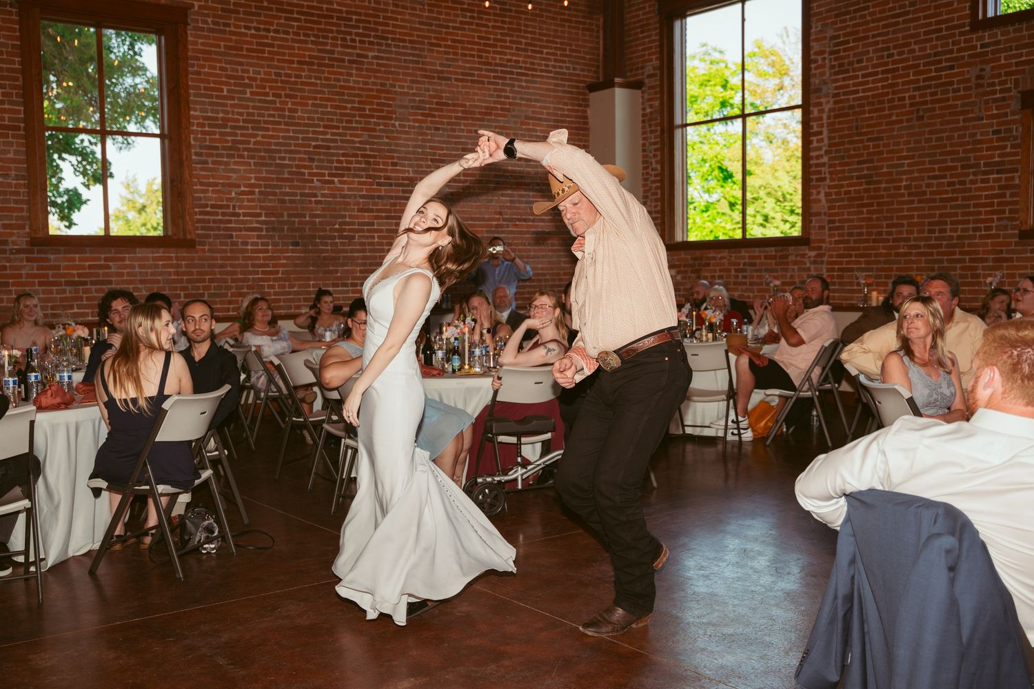 Wedding reception dancers perform synchronized moves in a rustic brick-walled event space.
