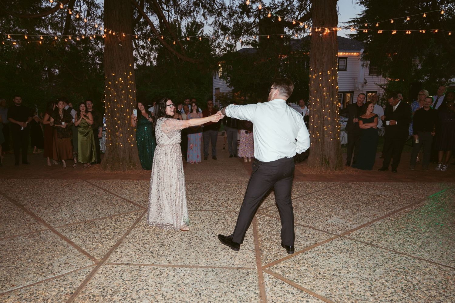 Evening wedding reception with string lights and guests dancing on a gravel dance floor.