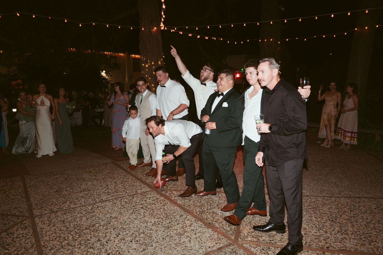Wedding guests dancing and celebrating on a gravel dance floor at night.