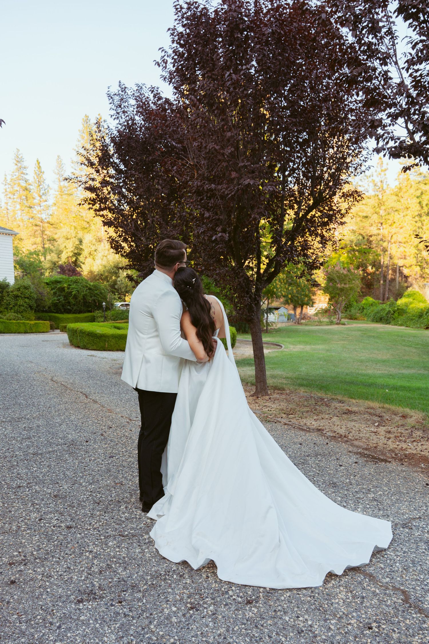 A wedding couple strolls through a garden setting with autumn trees and golden sunlight.