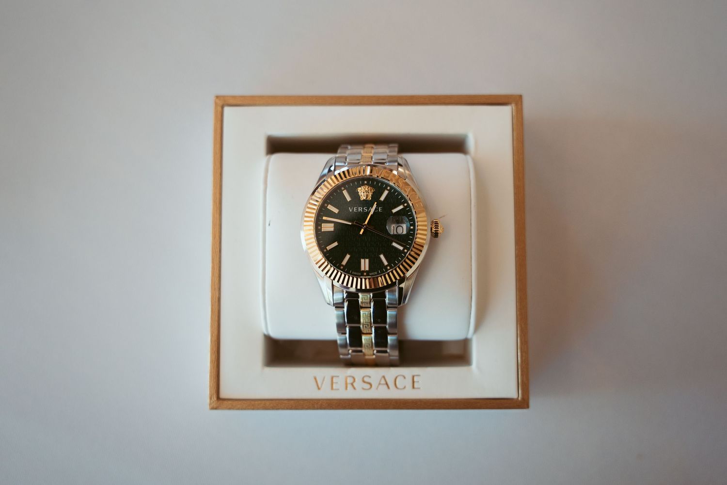 Luxury Versace watch displayed in a wooden frame against a neutral background.