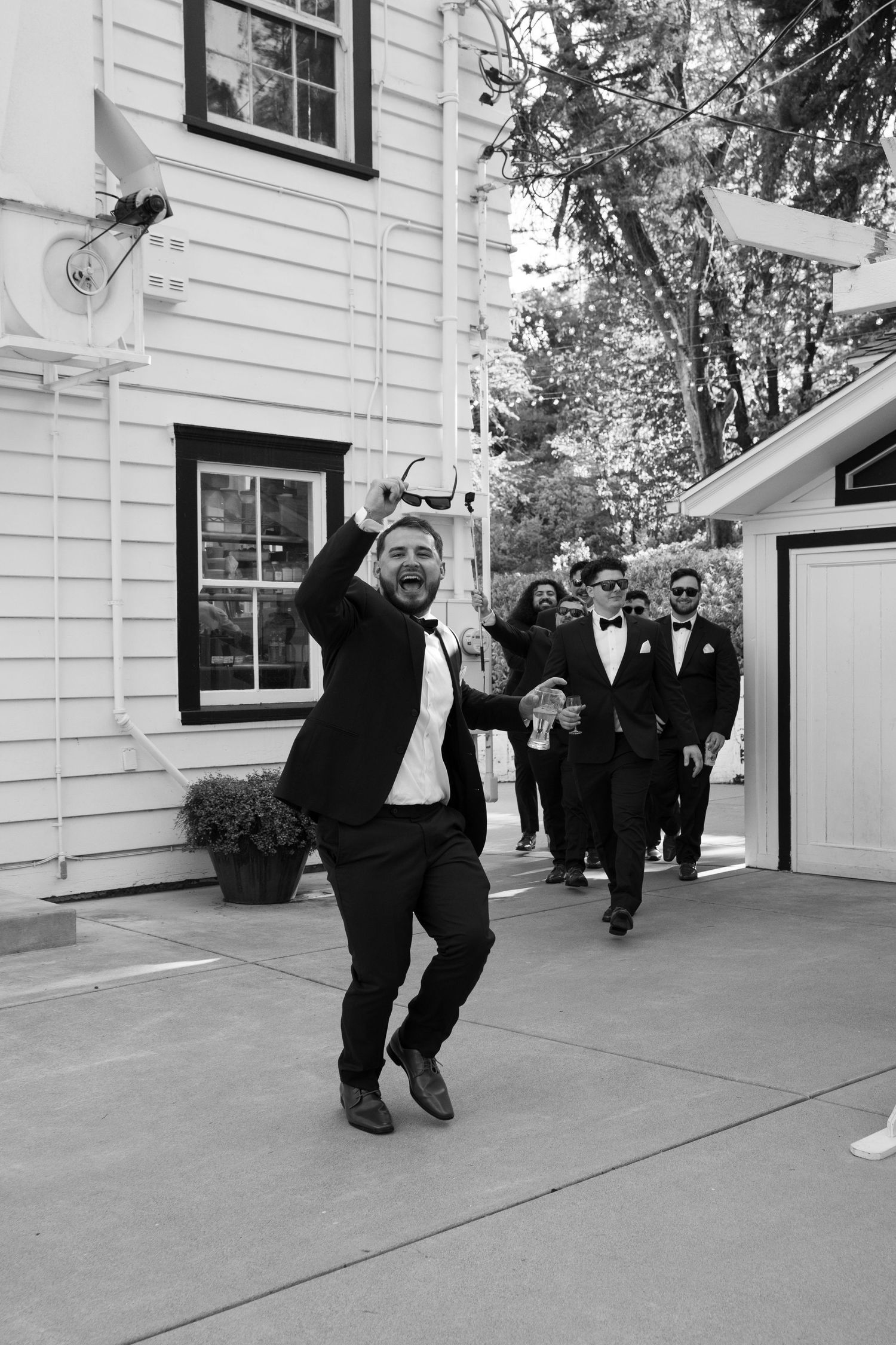 Person leaping joyfully outside a white building during a wedding celebration.
