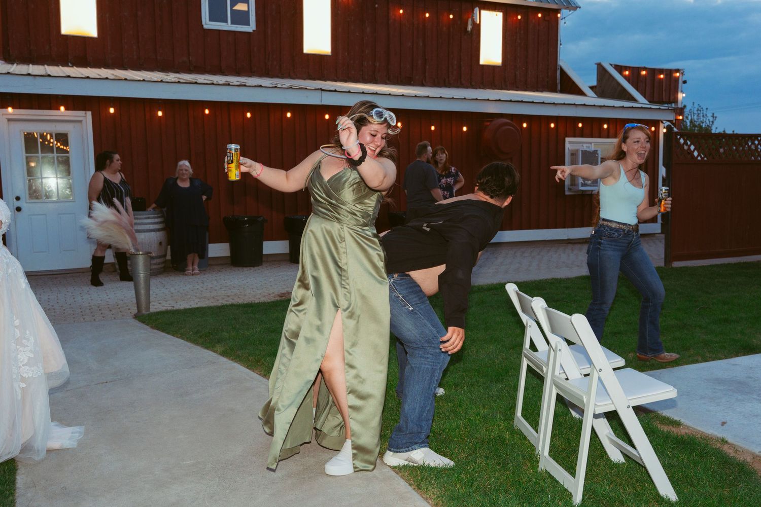 Wedding guests dancing and celebrating on an outdoor patio near a red barn at dusk.