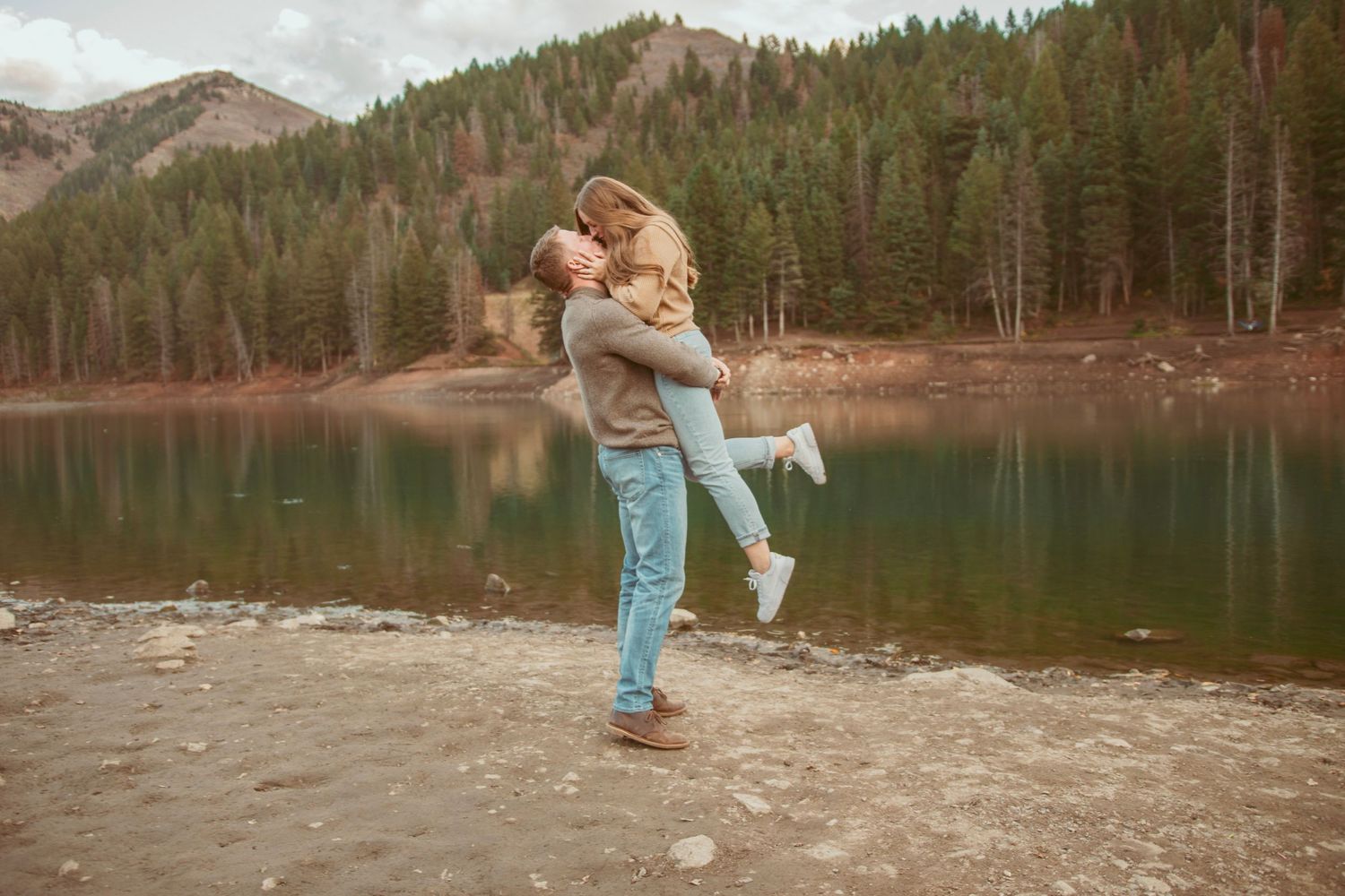 Romantic moment captured at a mountain lake as a couple embraces on the shoreline.