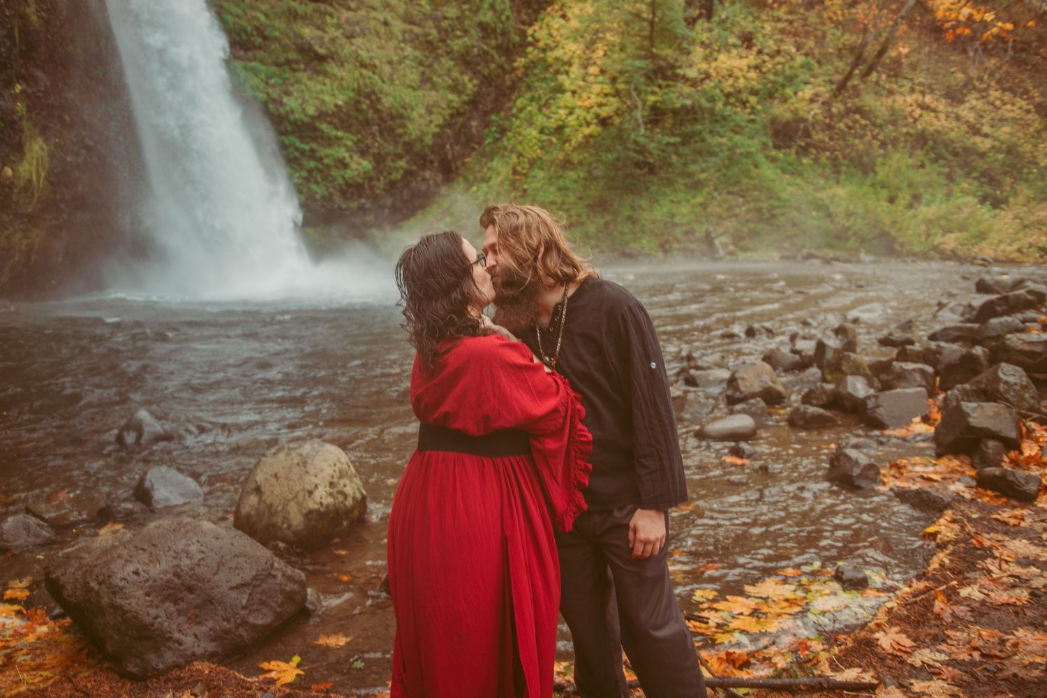 Romantic autumn photoshoot by a waterfall with dramatic red dress movement.