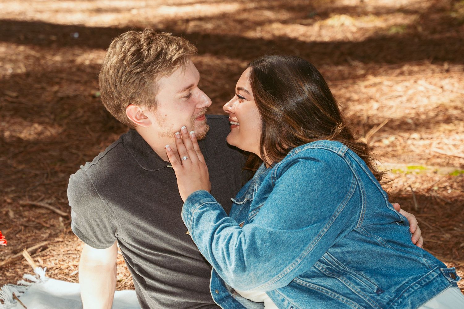 Two people sharing an intimate moment on a picnic blanket in a wooded area.