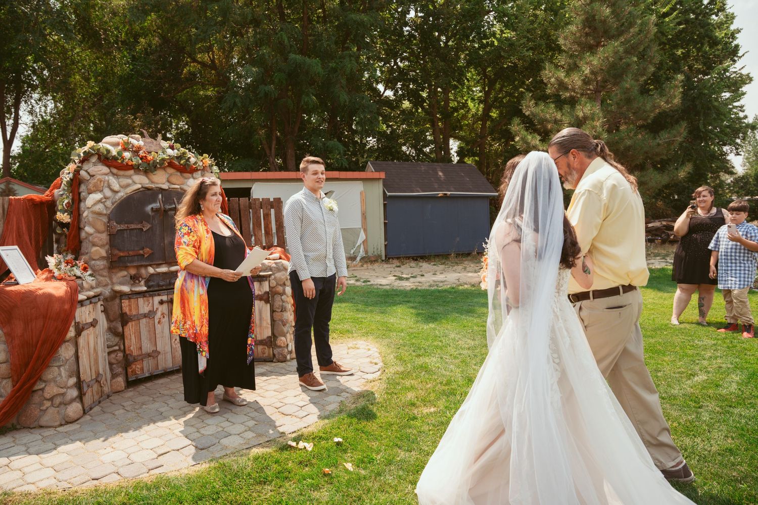 Panoramic view of a wedding celebration near stone walls and landscaped gardens.