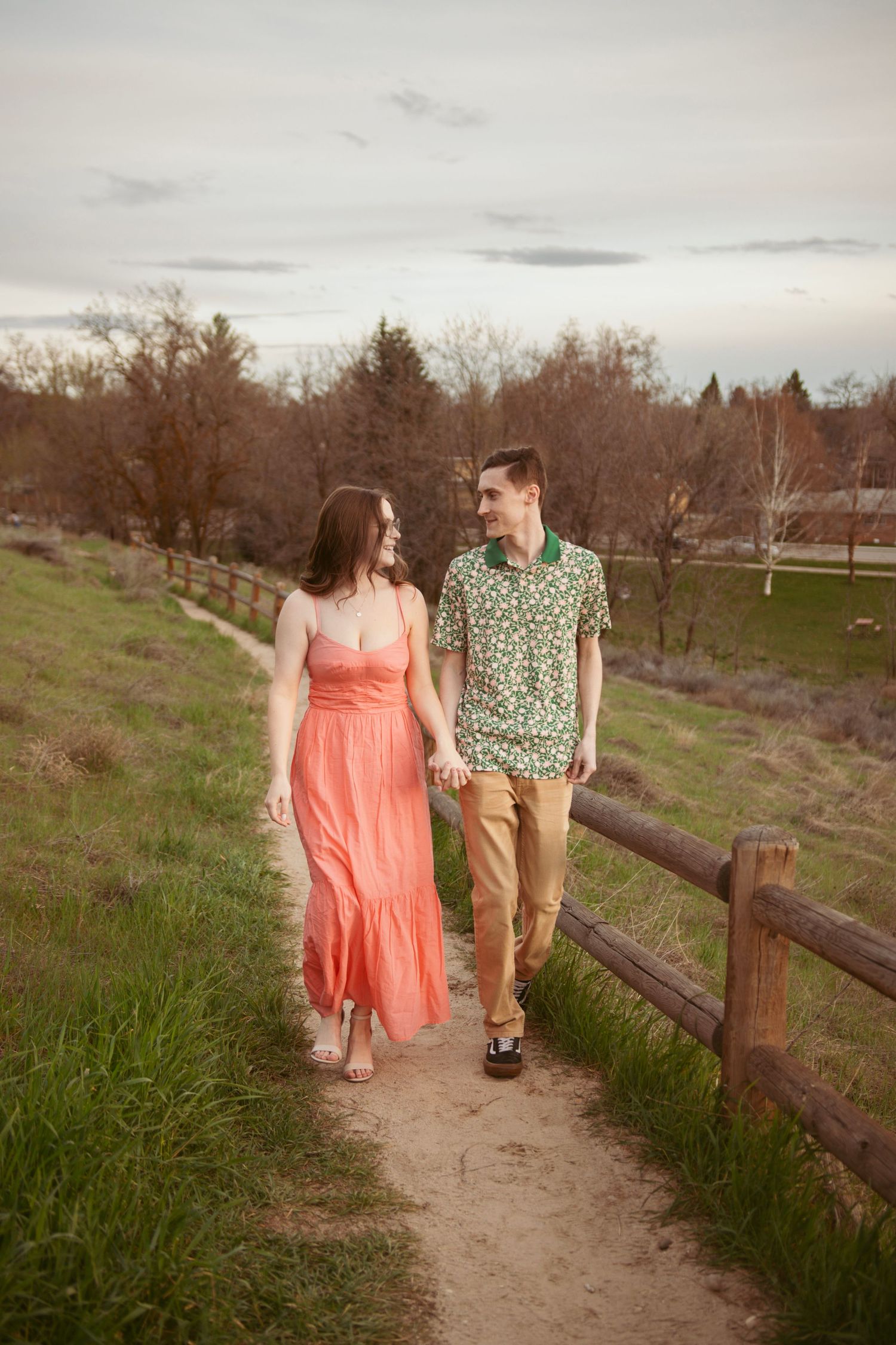 A couple walks hand in hand along a dirt path wearing spring outfits.