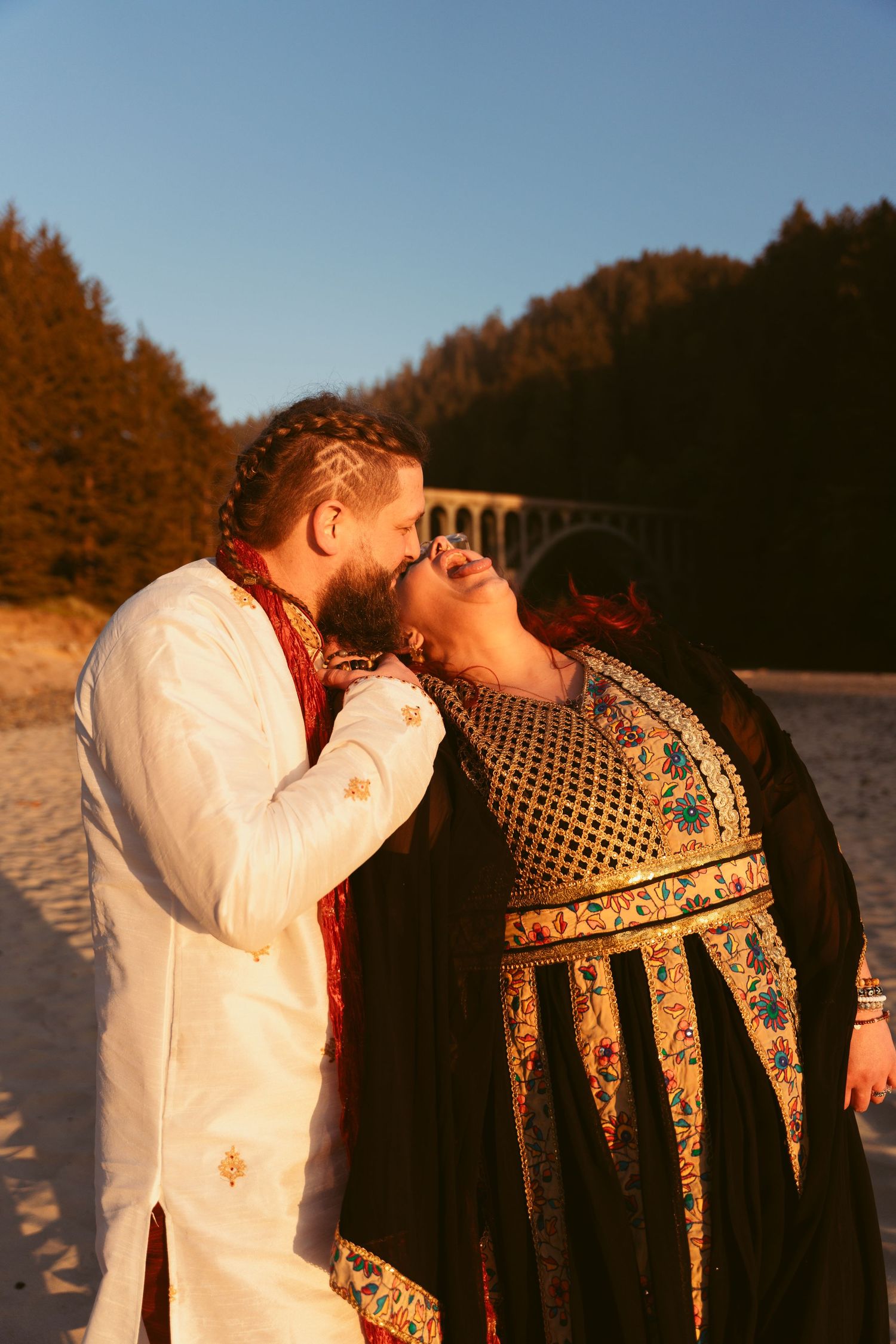 A joyful moment shared between two people in formal wear on a sandy beach at sunset.