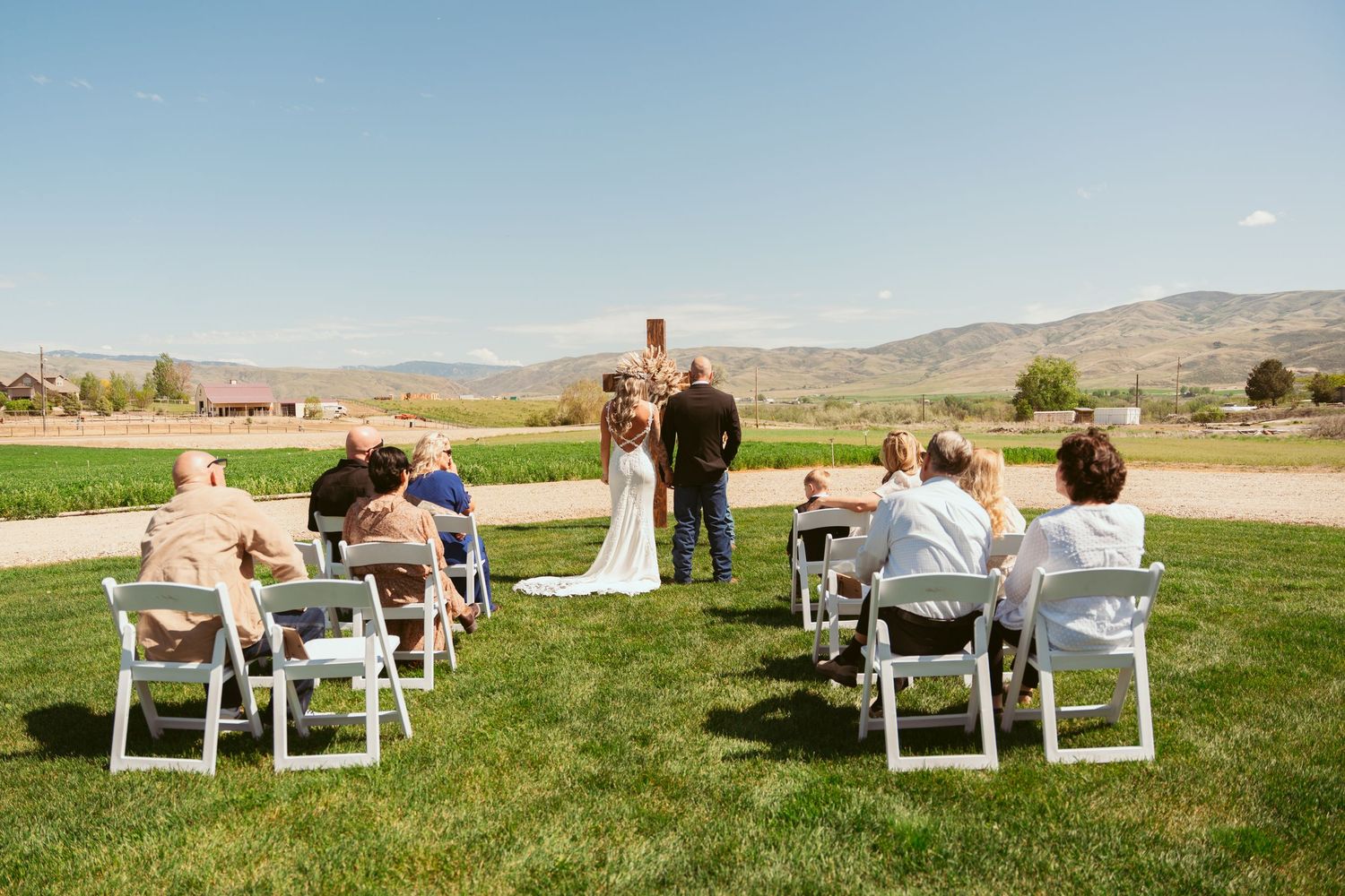 Panoramic view of wedding guests seated on white chairs with mountains and blue sky.