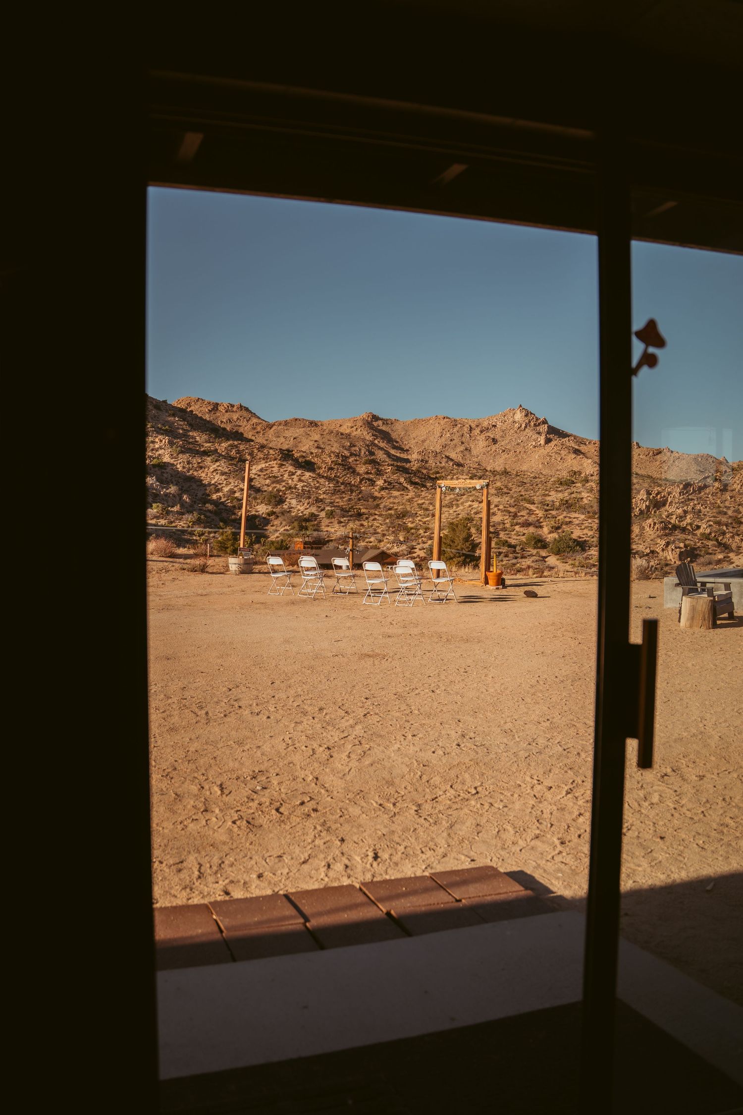 Desert landscape viewed through large windows showing white chairs arranged outdoors.