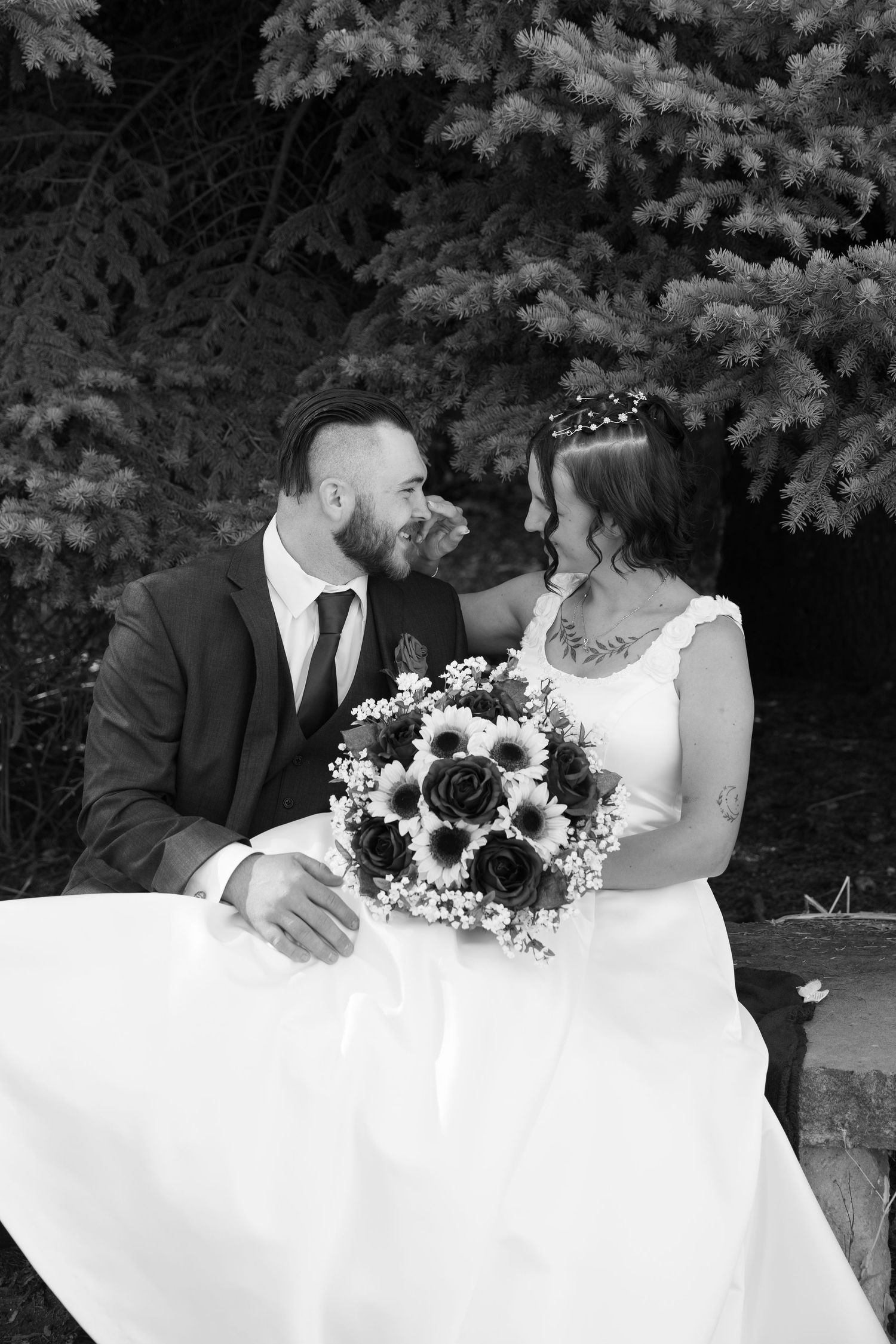 Artistic black and white wedding series with couple seated at table with floral arrangements.