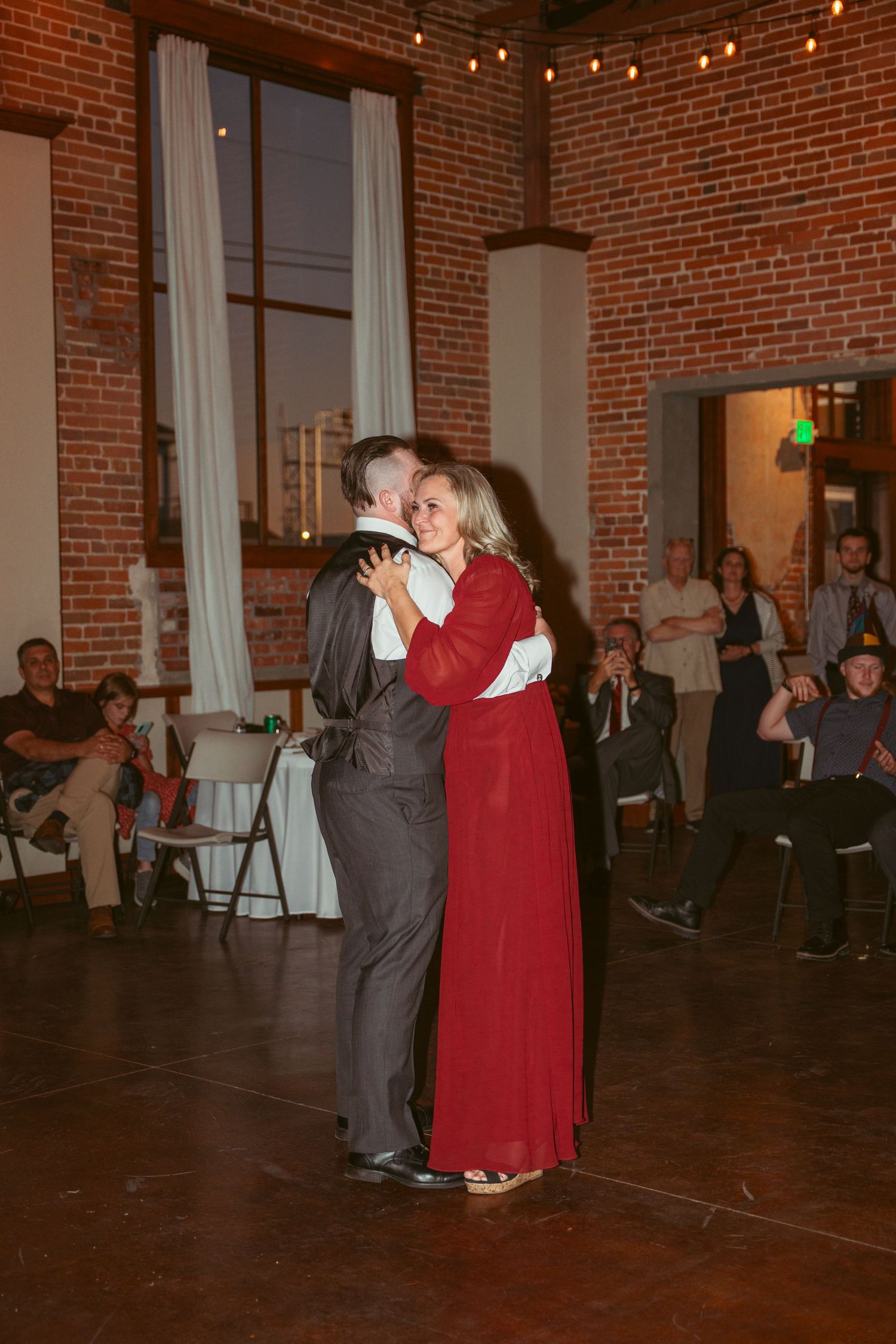 Wedding reception dance in a vintage brick venue with warm lighting and white drapes.