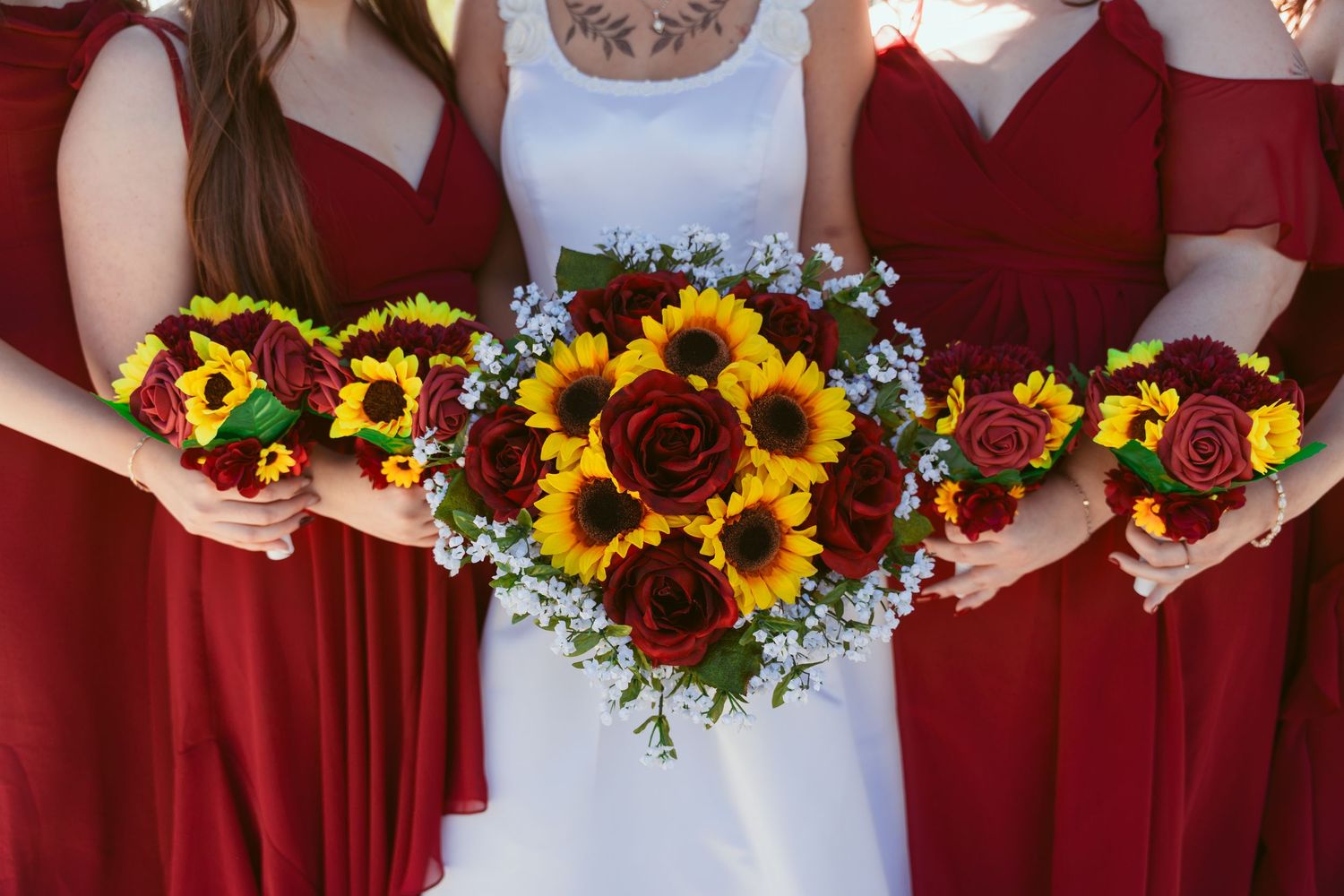 Close-up of vibrant sunflower and burgundy rose wedding bouquets held by bridesmaids.
