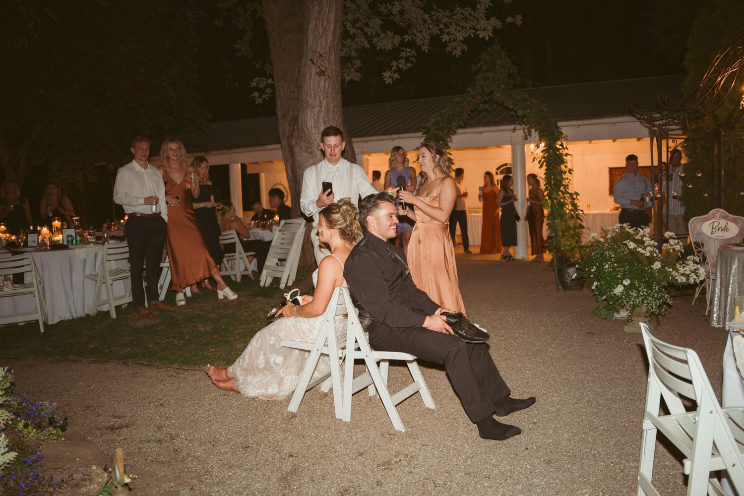 Outdoor wedding venue setup with white chairs and ambient lighting at night.
