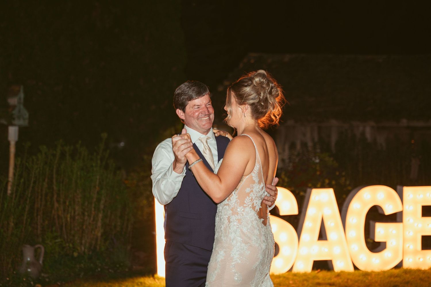 Romantic evening wedding scene with illuminated SAGE sign glowing in the background.