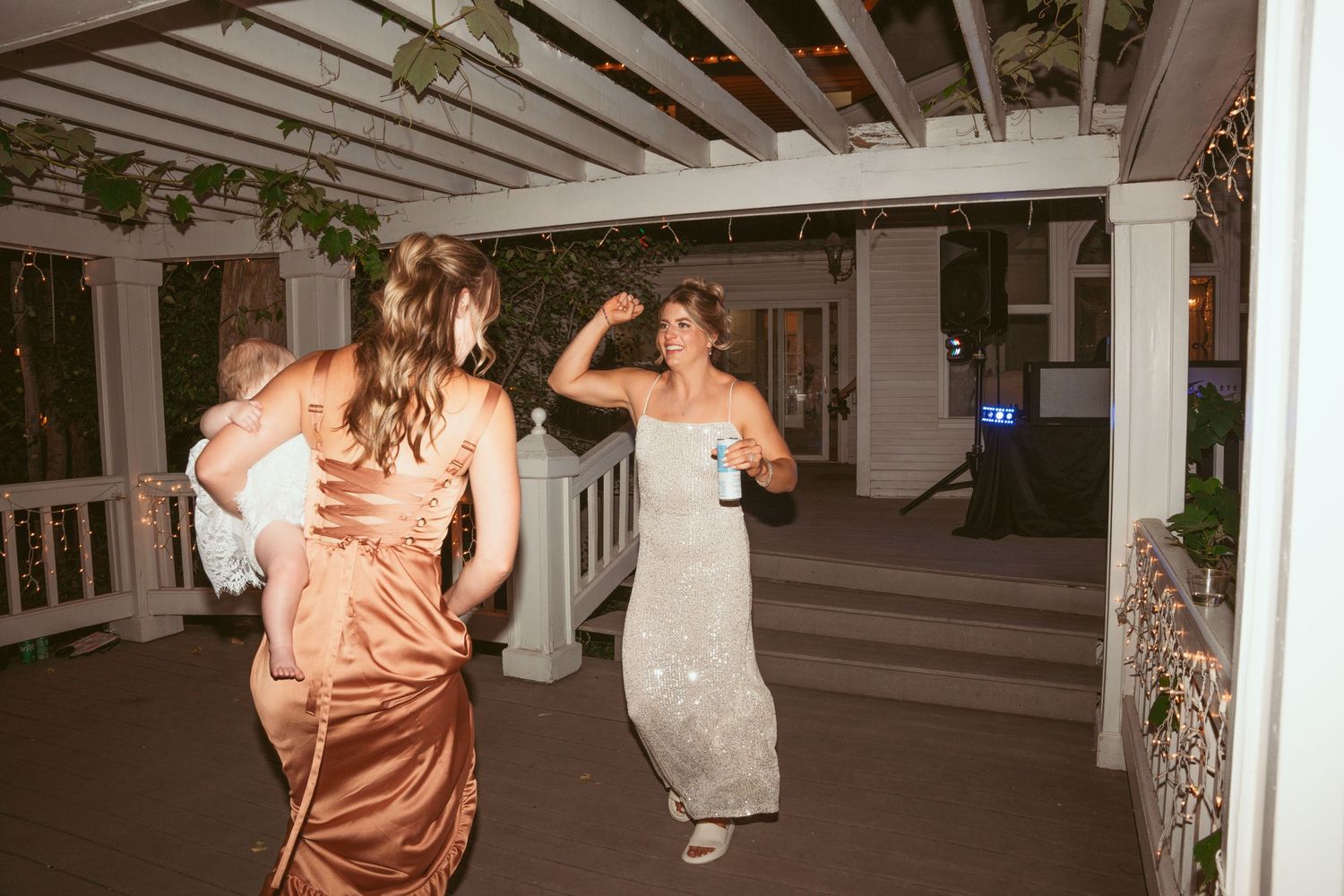 Wedding party dancing and celebrating in an elegant indoor venue with white decor and string lights.