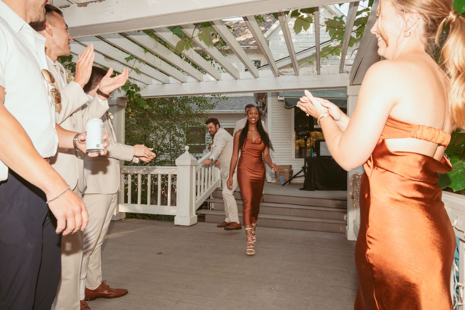 Wedding party members in orange dresses dancing together at an evening celebration.