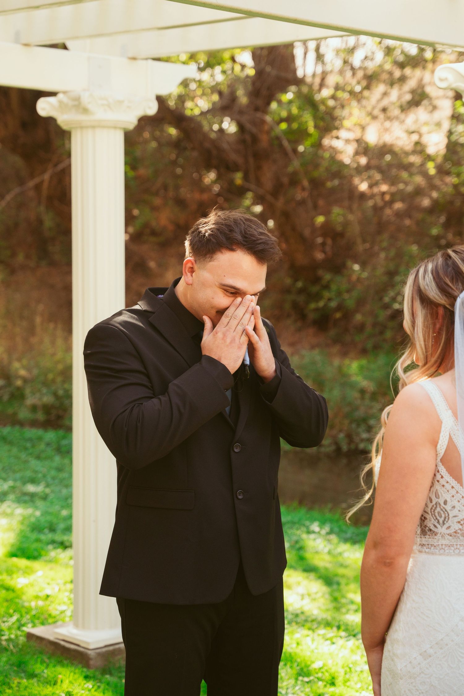 Emotional first look moment between couple during outdoor wedding ceremony with white gazebo pillars.