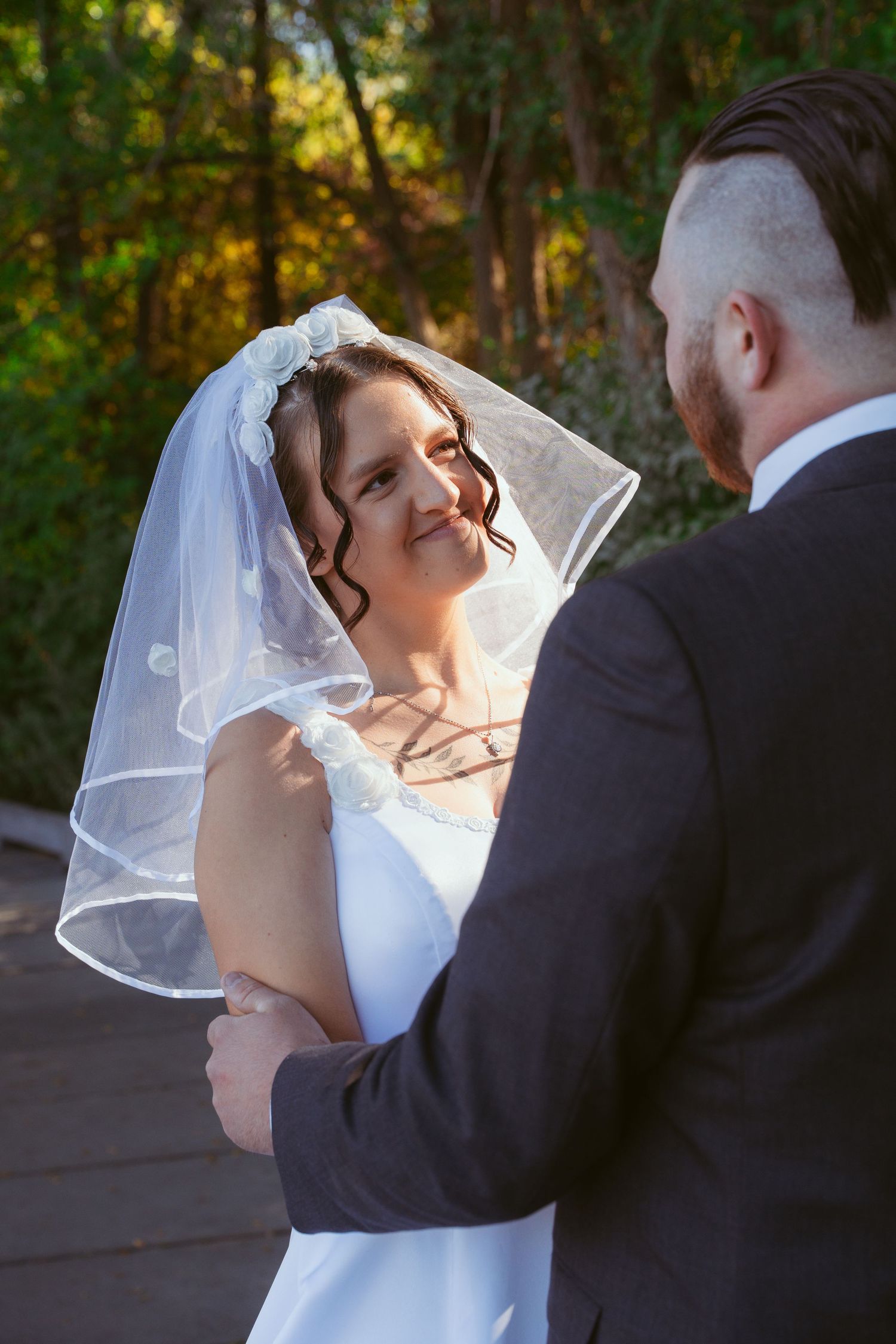 Wedding couple sharing a romantic moment outdoors with a white veil flowing in the breeze.
