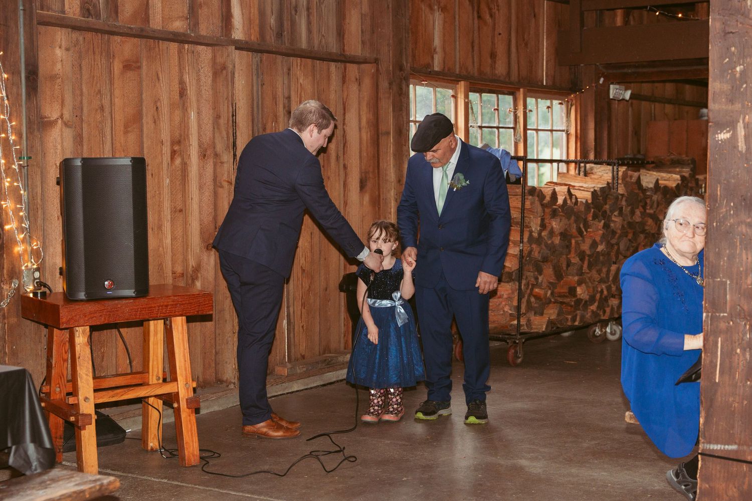 Wedding guests gather in a rustic wooden barn decorated with string lights for a celebration.