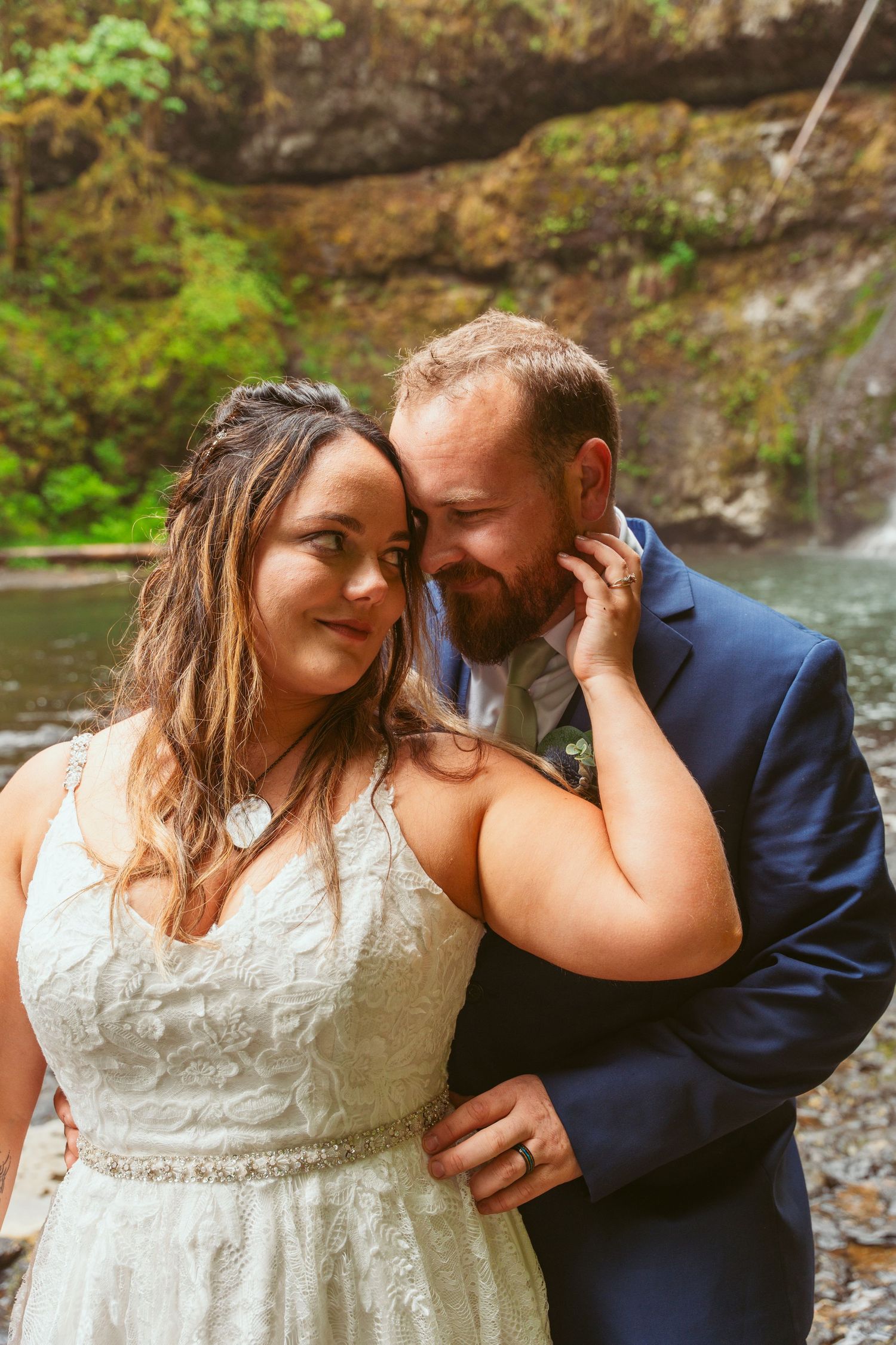 Tender moment between newlyweds during their forest waterfall photoshoot.