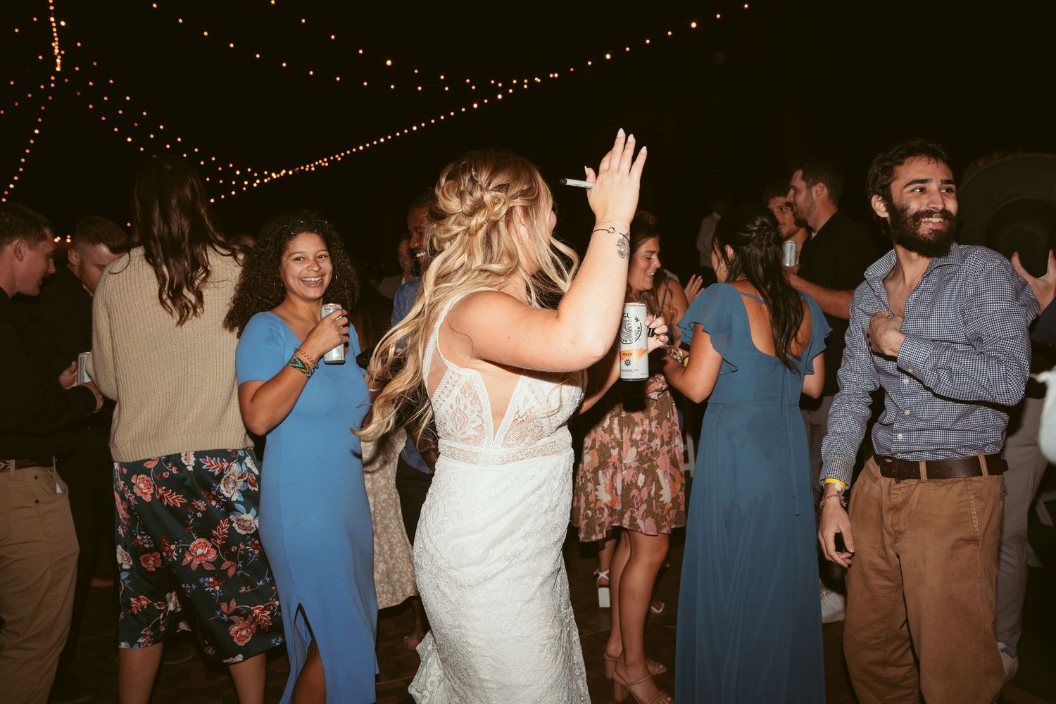 Crowded dance floor at wedding reception with guests dancing under warm string lights.