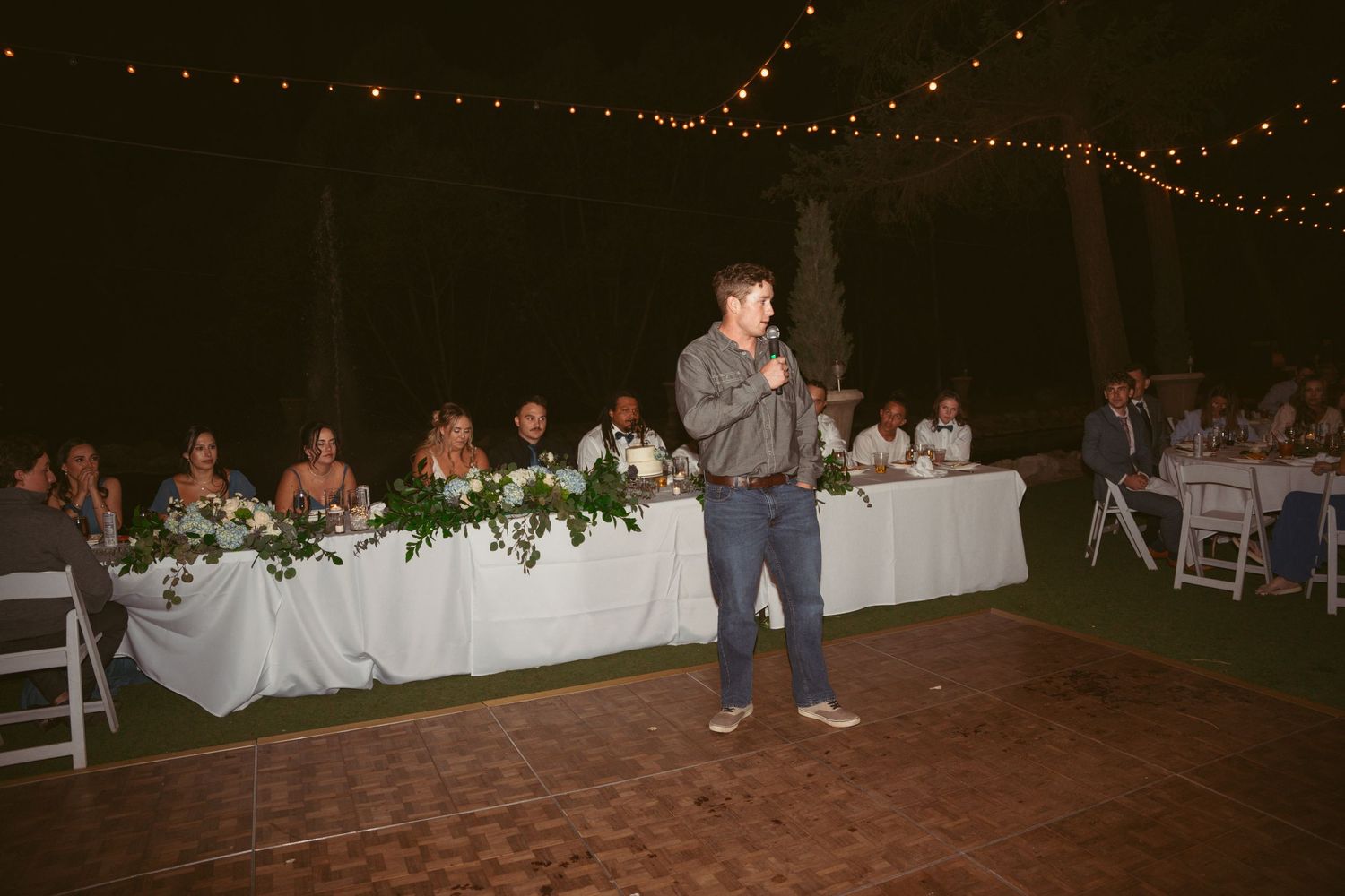 Evening wedding reception with guests seated at decorated tables under ambient lighting.